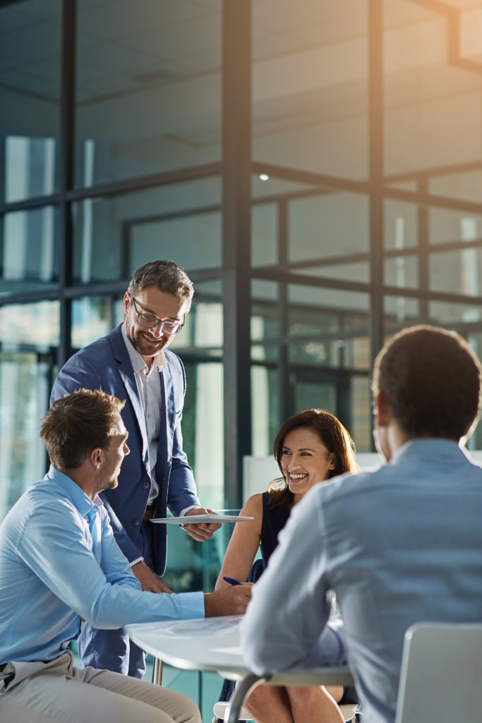 A group of business professionals engaged in a meeting around a conference table in a modern office setting.