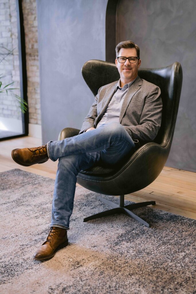 Jeff Metzger sitting comfortably in an armchair, gazing out of a window with natural light streaming in.